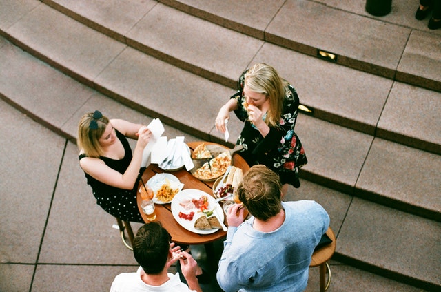 Tri ženy sedia pri stole a obedujú.jpg